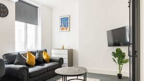 A modern living room with a grey sofa, round coffee table, and a potted plant. - Edgware Road Apartments (London)