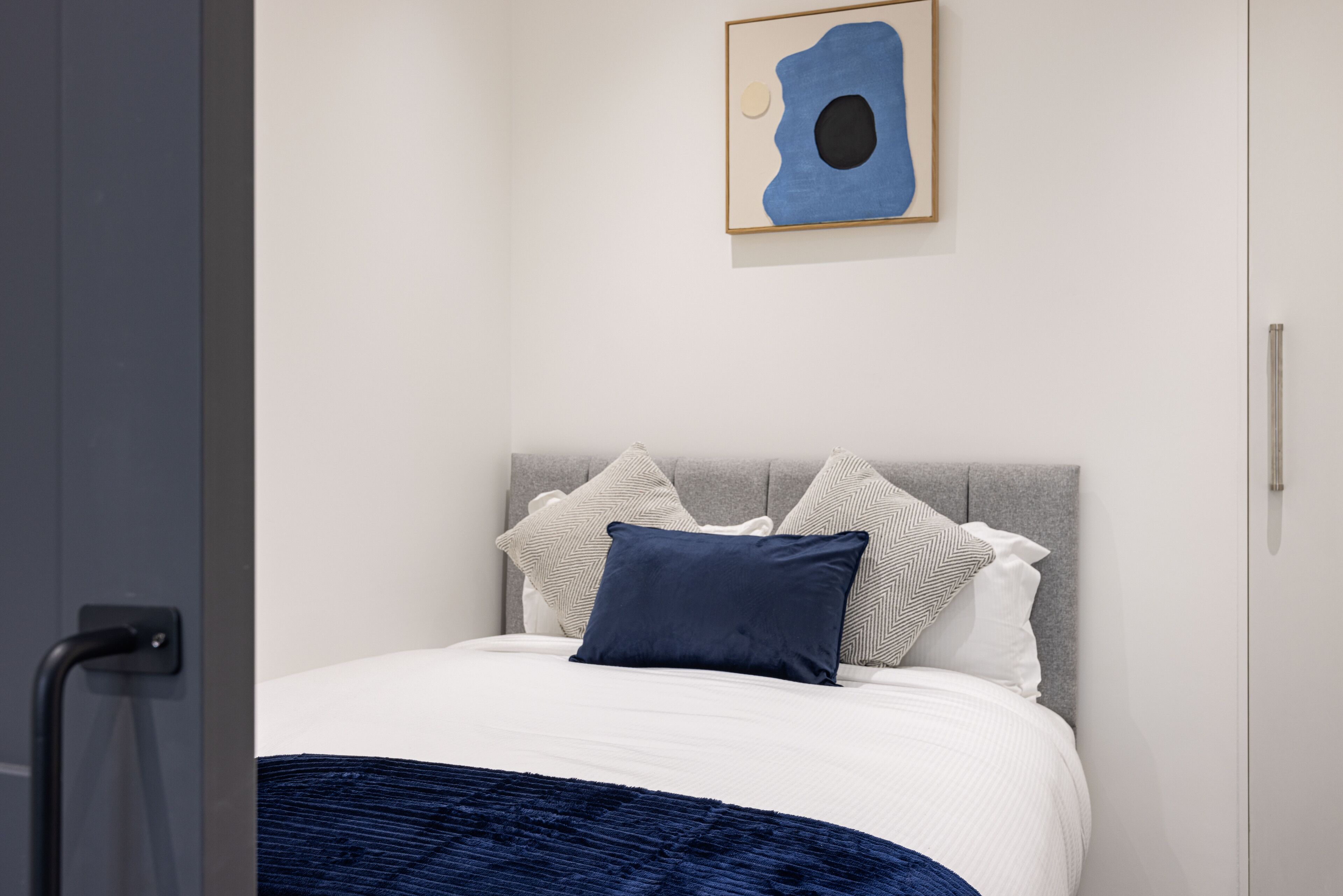Una camera da letto moderna con un letto, cuscini e un quadro astratto appeso al muro.