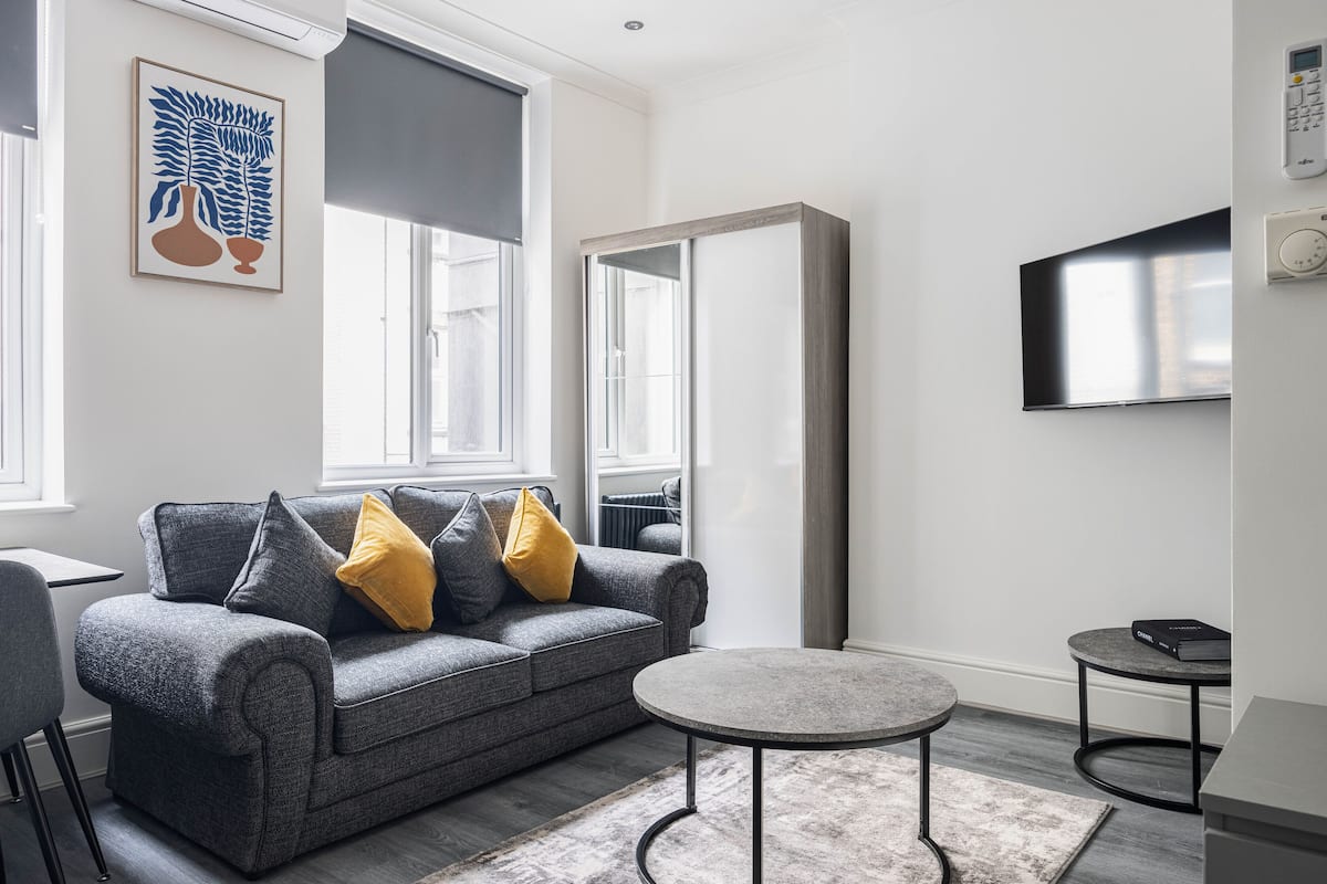 Un salon moderne avec un canapé gris, une table basse ronde et un téléviseur à écran plat fixé au mur.