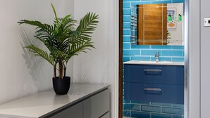 A bathroom with a blue-tiled wall, a white sink, and a potted plant. - Edgware Road Apartments (London)