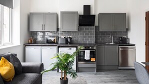 A modern kitchen with grey cabinets, a black range hood, and stainless steel appliances. - Edgware Road Apartments (London)