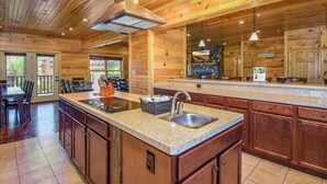 A spacious kitchen with wooden cabinets, a granite countertop, and a large island with a sink. - Free Tickets | 2 Hot Tubs, Arcade, Fireplace, Parking, Easy Access for Buses (Gatlinburg)