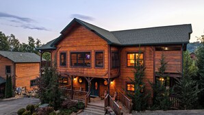 A two-story wooden cabin with a porch, a staircase, and a small outdoor seating area. - Free Tickets | 2 Hot Tubs, Arcade, Fireplace, Parking, Easy Access for Buses (Gatlinburg)