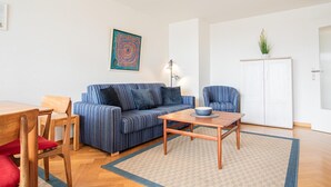 A living room with a striped sofa, a wooden coffee table, a blue armchair, and a cabinet. - App. Bagehorn 10 (Westerland)