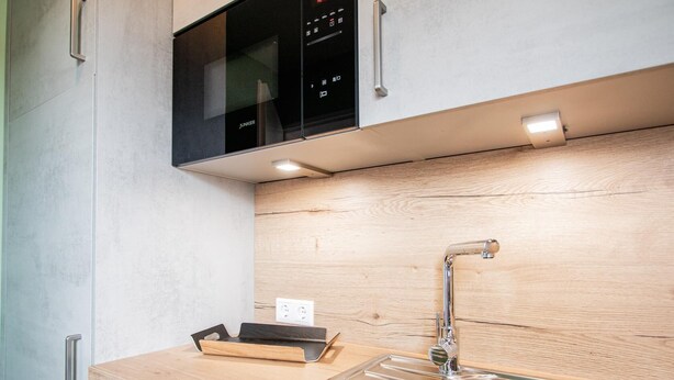 A modern kitchen with a stainless steel sink, wooden countertop, and a black microwave above the counter. - App. Bagehorn 10 (Westerland)