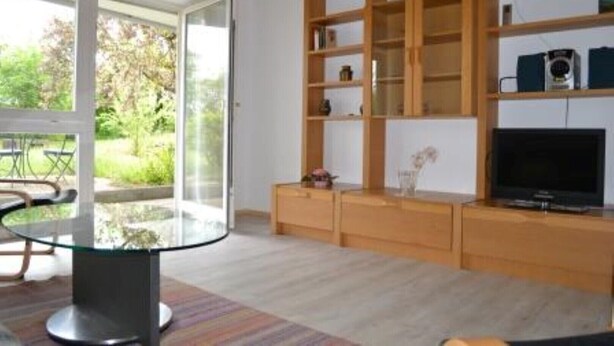Een moderne woonkamer met een glazen tafel, houten planken en een televisie.