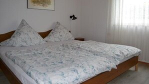 Een slaapkamer met een bed, twee kussens, een nachtkastje en een wandlamp.