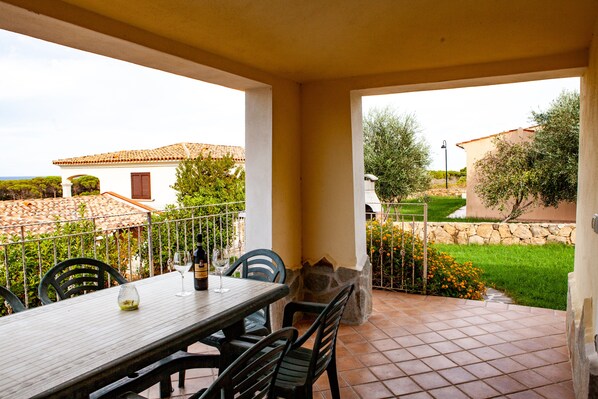 An outdoor patio with a table and chairs, a stone wall, and a view of a house with a tiled roof.