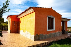A single-story house with a tiled patio, a small garden, and a clear sky.
