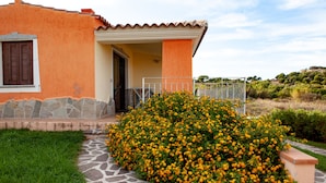 A house with a stone pathway leading to the entrance, surrounded by a well-maintained garden with yellow flowers. - FANTASTICO PEDRAMI 1 (Budoni)
