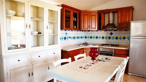 A kitchen with wooden cabinets, a white refrigerator, and a dining table with chairs. - FANTASTICO PEDRAMI 1 (Budoni)