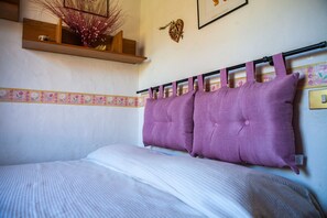 A bedroom with a bed, a headboard with multiple pillows, a shelf with decorative items, and a wall with a heart-shaped decoration.