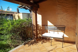 A patio with a metal bench, a tiled floor, and a wall with a window.