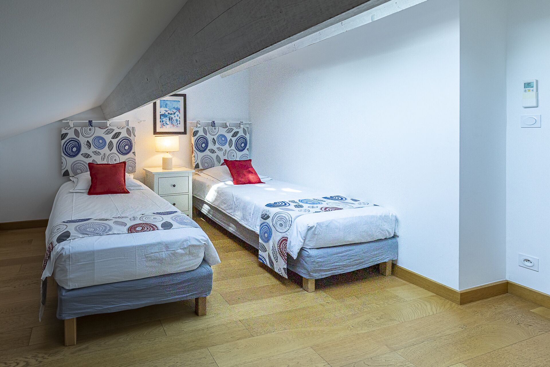 A bedroom with two single beds, a nightstand, a lamp, and a framed picture on the wall.