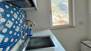 A kitchen with a sink, a window with a view of a mountainous landscape, and a patterned backsplash. - Villa with a spectacular view,  in a peaceful location, very romantic, (Positano)