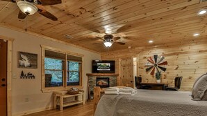 A cozy log cabin bedroom with a bed, a fireplace, a television, and a large window. - ​​​​​​​Jagged Owl by Mountain Oasis | Dog-Friendly Cabin in Coosawattee River Resort (Ellijay)