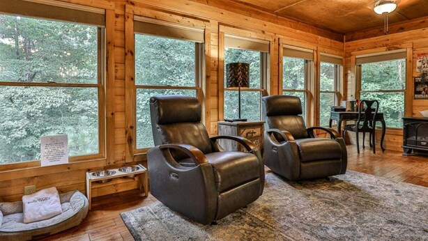 A cozy cabin interior with two leather recliners, a pet bed, a fireplace, and large windows offering a forest view. - ​​​​​​​Jagged Owl by Mountain Oasis | Dog-Friendly Cabin in Coosawattee River Resort (Ellijay)