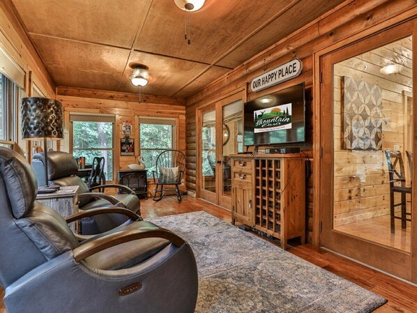 A cozy cabin interior with leather recliners, a television, and a 'Our Happy Place' sign.