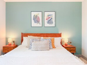 A neatly made bed with a wooden headboard, two bedside tables with lamps, and two framed artworks on the wall. - Resort-Style Condo 3 Miles to Disney (Fullerton)