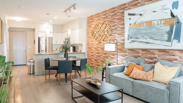 A modern living room with a grey sofa, a coffee table, and a dining area with chairs and a table. - Resort-Style Condo 3 Miles to Disney (Fullerton)