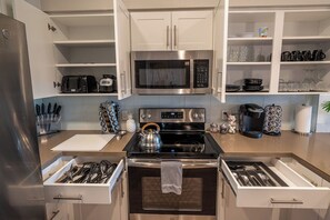 A modern kitchen with white cabinetry, a stainless steel refrigerator, a microwave, a stove, and a coffee maker. - Resort-Style Condo 3 Miles to Disney (Fullerton)