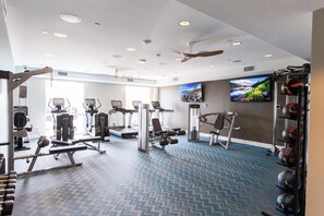 Une salle de sport équipée de matériel d’exercice, d’un téléviseur et d’un ventilateur de plafond.
