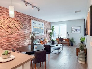 A modern living room with a wooden accent wall, a dining area with a round table, and a seating arrangement. - Resort-Style Condo 3 Miles to Disney (Fullerton)