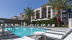 A swimming pool with lounge chairs and umbrellas, surrounded by multi-story buildings. - Resort-Style Condo 3 Miles to Disney (Fullerton)