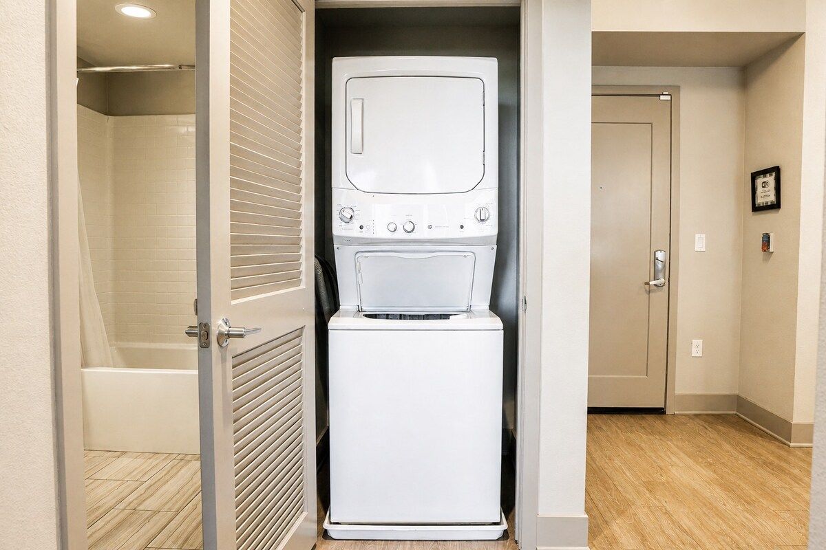 A compact laundry room with a washing machine and dryer, a shower area, and a door leading to another room.
