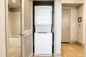 Une petite buanderie comprenant un lave-linge et un sèche-linge, un espace douche et une porte donnant sur une autre pièce.