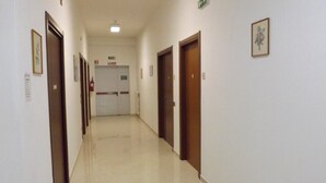 A hallway with doors on both sides, a fire exit sign, and a ceiling light. - Ostello Il Volto (Potenza)