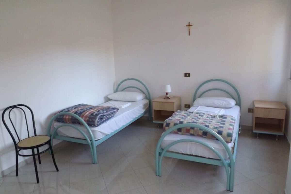 A bedroom with two single beds, a chair, bedside tables, and a cross on the wall.