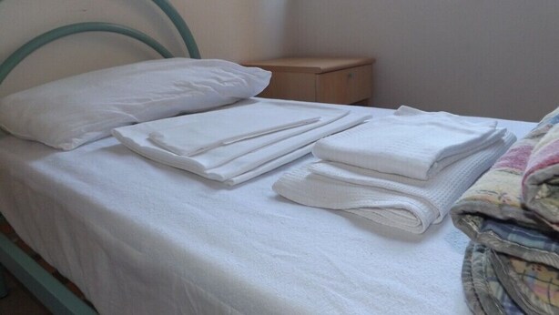 A single bed with a metal headboard, a wooden nightstand, and a window with blinds. - Ostello Il Volto (Potenza)
