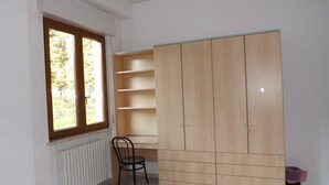 A room with a large wardrobe, a chair, and a window with a view of trees. - Ostello Il Volto (Potenza)