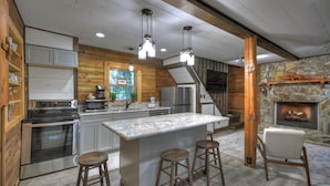 Una cocina moderna con una isla grande, taburetes de bar, una chimenea de piedra y un interior de madera.