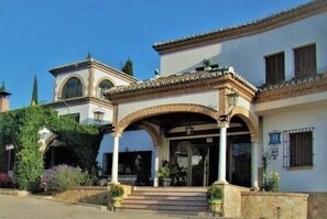 A traditional building with a tiled roof, arched entrance, and a small tower-like structure. - Hotel Escua (Archidona)