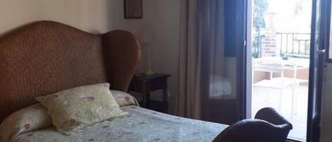 Un dormitorio con cama, una silla, una mesita de noche y una ventana con cortinas.