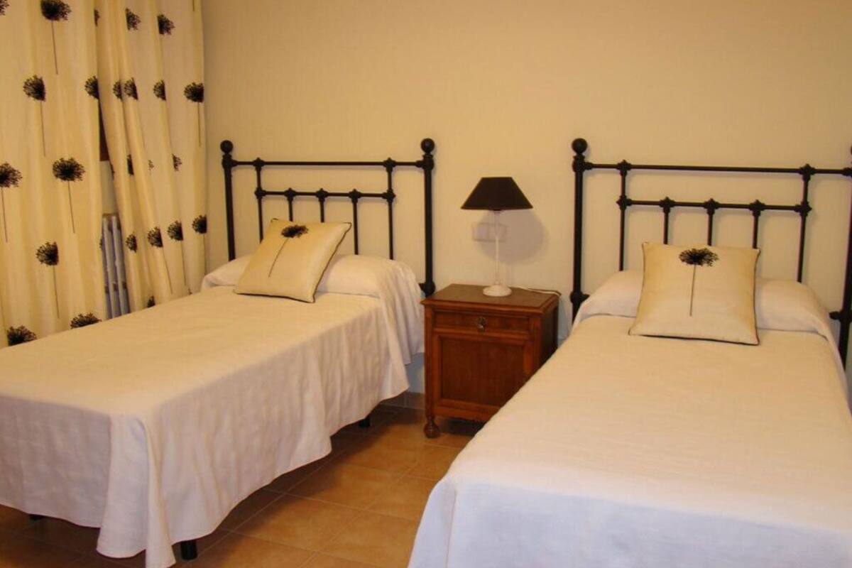 A room with two single beds, each with a pillow and a nightstand with a lamp.