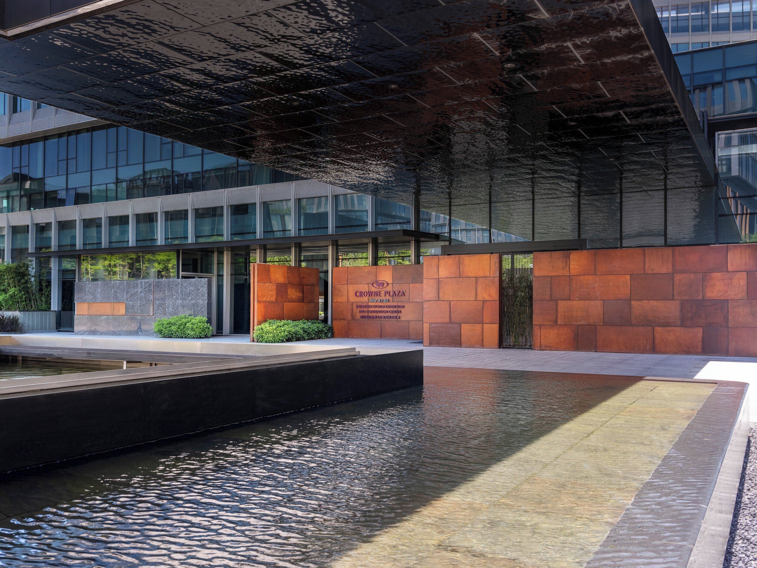 Un edificio moderno con fachada de vidrio reflectante, una fuente de agua y un cartel que dice 'CROWN PLAZA'.