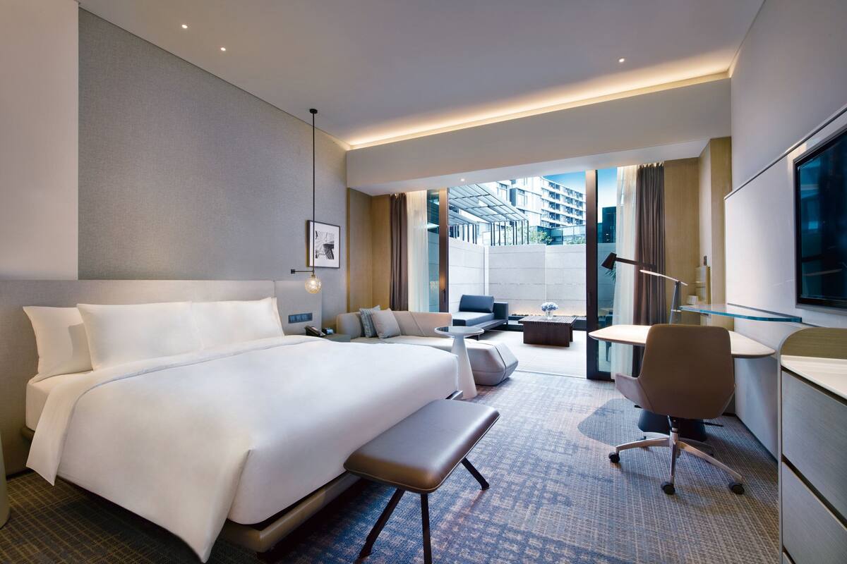 Une chambre d’hôtel moderne dotée d’un grand lit, d’un coin salon avec un canapé et des fauteuils, d’une petite table et d’un bureau.
