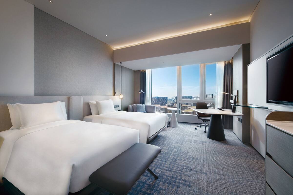 Une chambre d’hôtel avec deux lits, un bureau, une télévision et une vue sur la ville.