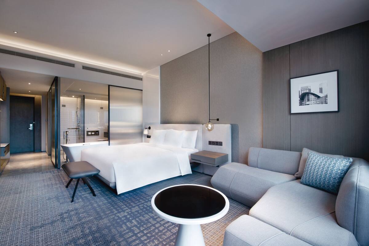 Une chambre d’hôtel moderne avec un grand lit, un canapé, une petite table et un tableau au mur.