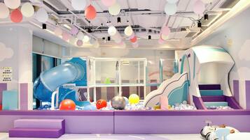 A children's play area with a slide, climbing net, and ball pit.