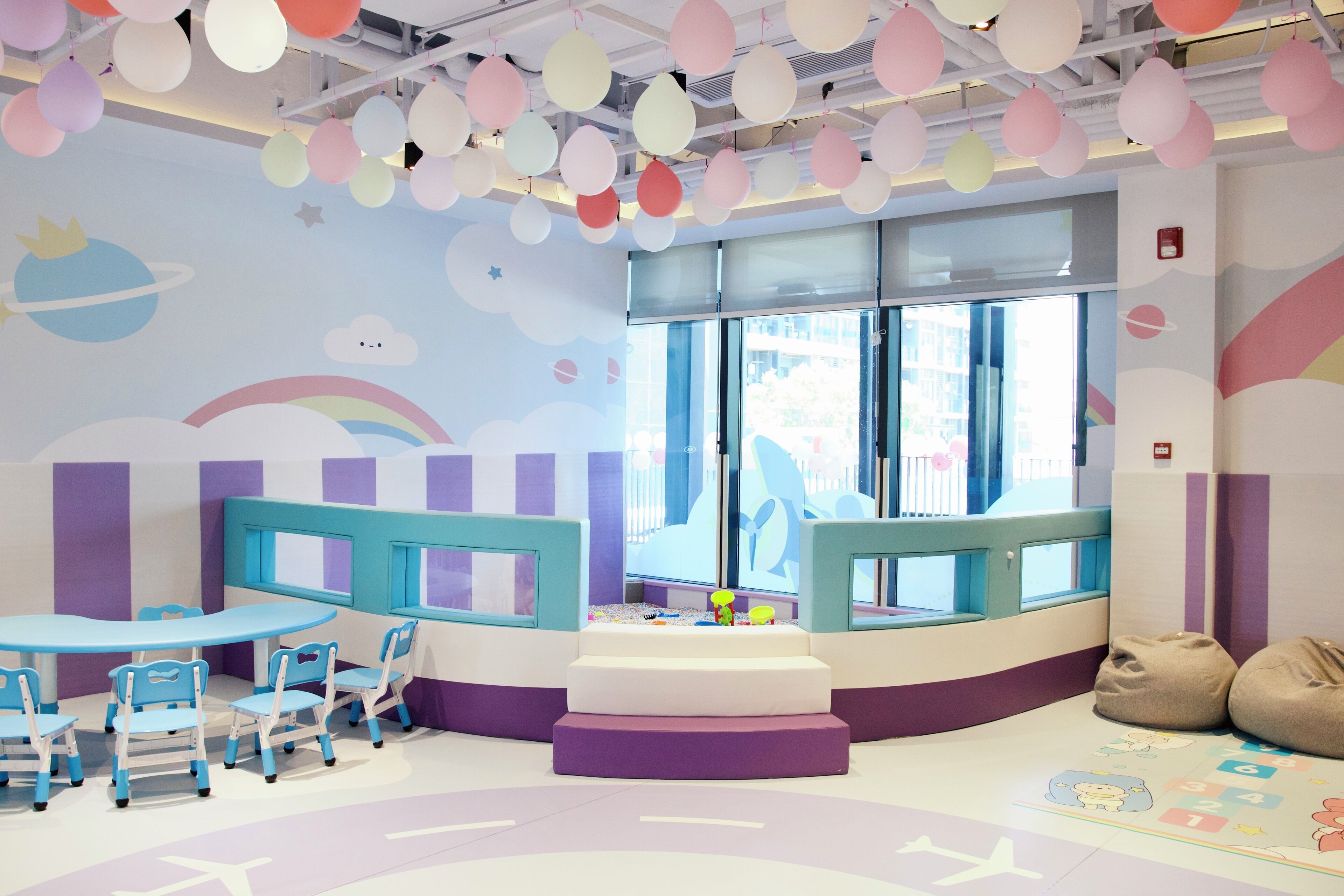 Zona infantil con una mesa redonda, sillas, pufs y un colorido mural.