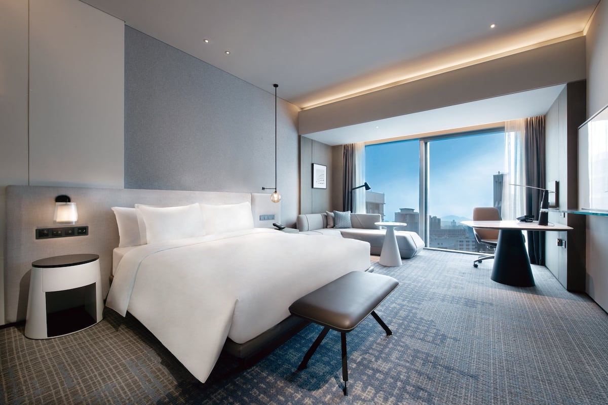 Une chambre d’hôtel moderne, dotée d’un grand lit, d’un bureau, d’une chaise et offrant une vue sur la ville.