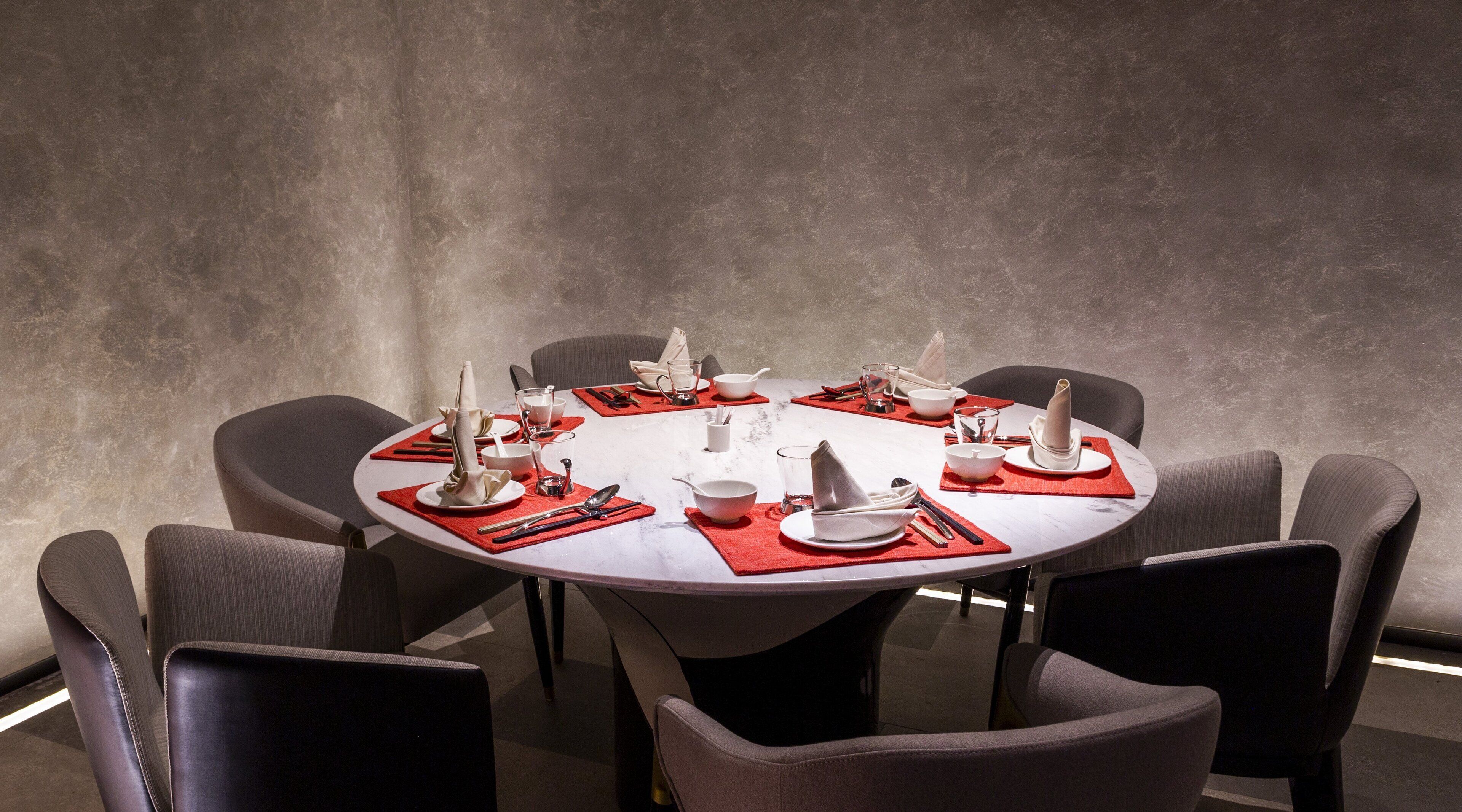 A round dining table with red placemats, white plates, and silverware, surrounded by dark upholstered chairs.