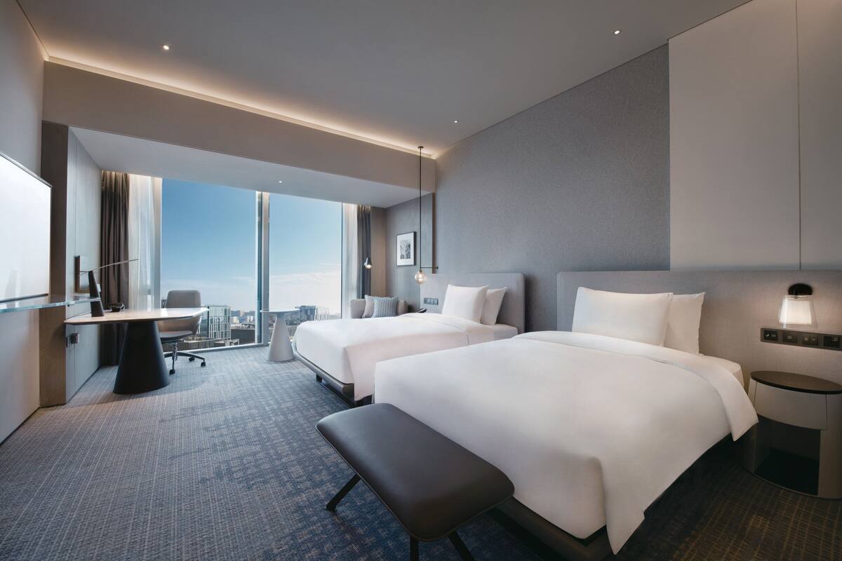Une chambre d’hôtel moderne avec deux lits, un bureau et une vue sur la ville.