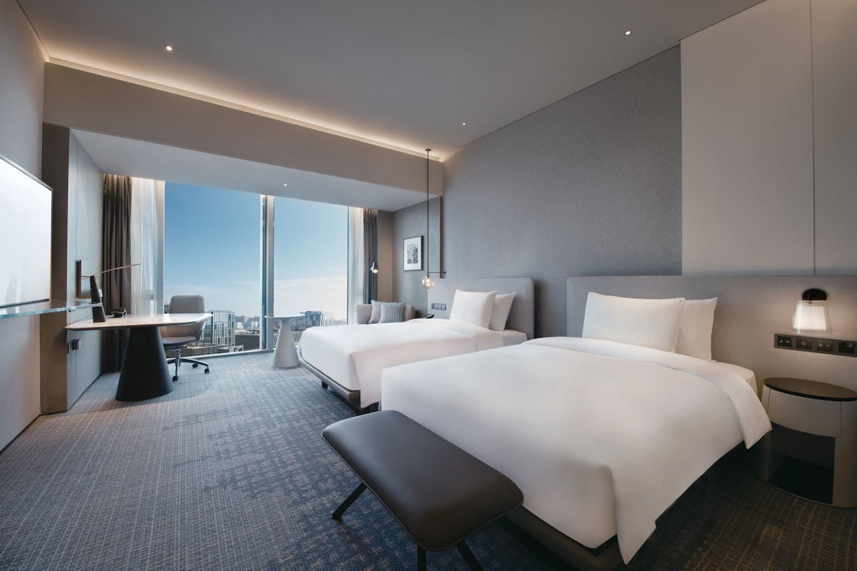 Ett modernt hotellrum med två sängar, ett skrivbord och utsikt över staden.