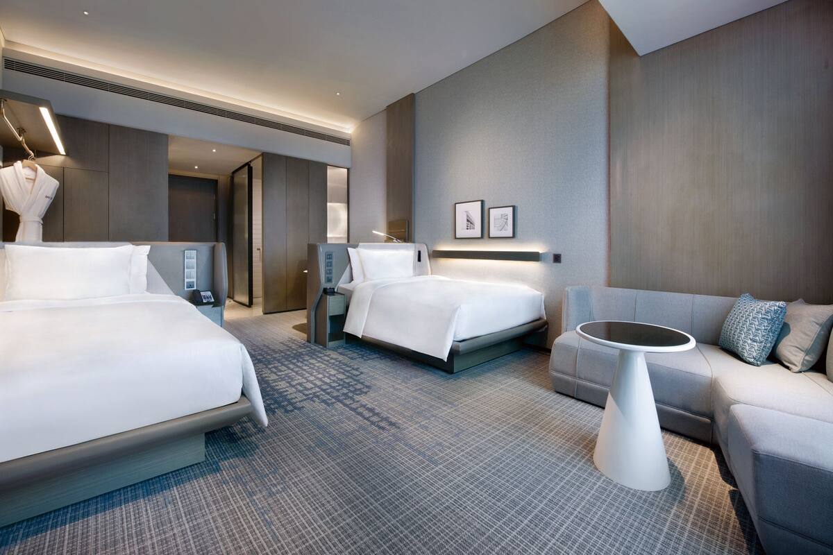 Une chambre d’hôtel moderne équipée de deux lits, d’un canapé, d’une petite table et d’un porte-peignoir.