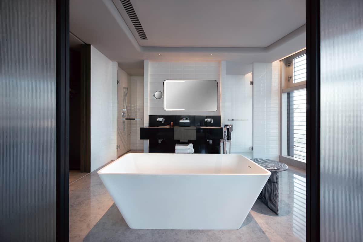 A modern bathroom with a large freestanding bathtub, a mirror above the sink, and a window providing natural light.